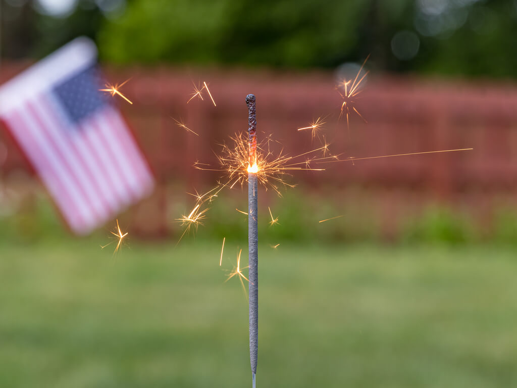sparkler burning in yard with american flag in background