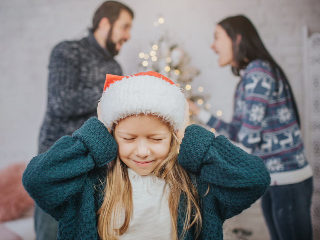 little girl in a santa hat blocking out her parents arguing