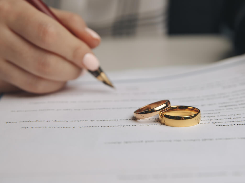woman signing legal documents with wedding rings on top
